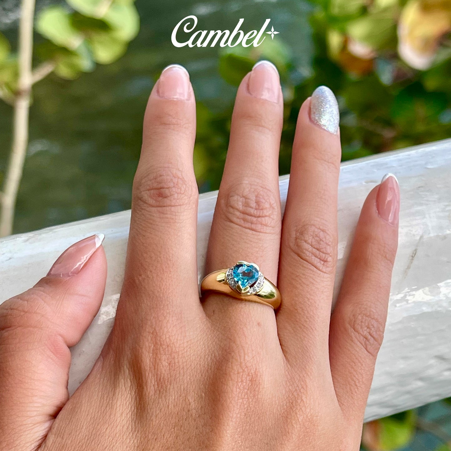 Fotografía en detalle de Anillo de diseño corazón en mano delicada de oro de 18k con un majestuoso topacio Swiss Blue natural y diamantes, alta joyería de Cambel